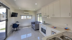 A modern kitchen with white cabinets, a gas stove, and a dining area with a table and chairs. - Swan Hill Lifestyle Park (Swan Hill)
