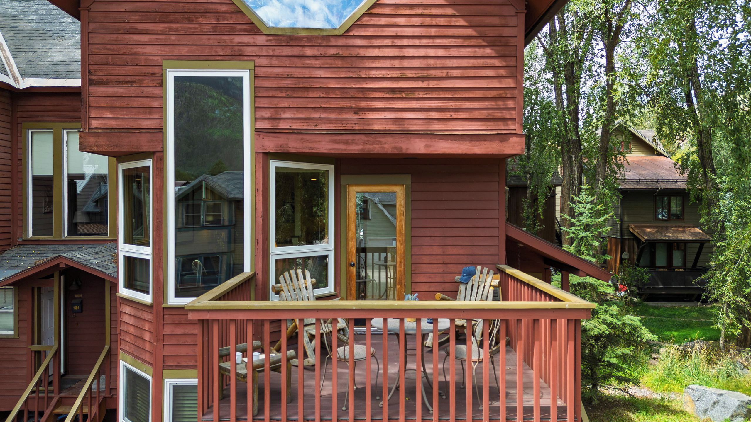 Een rode houten woning met een terras, meerdere ramen en een zichtbare trap.