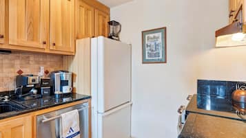 Una cocina compacta con armarios de madera, un refrigerador blanco, una cafetera y un hervidor.