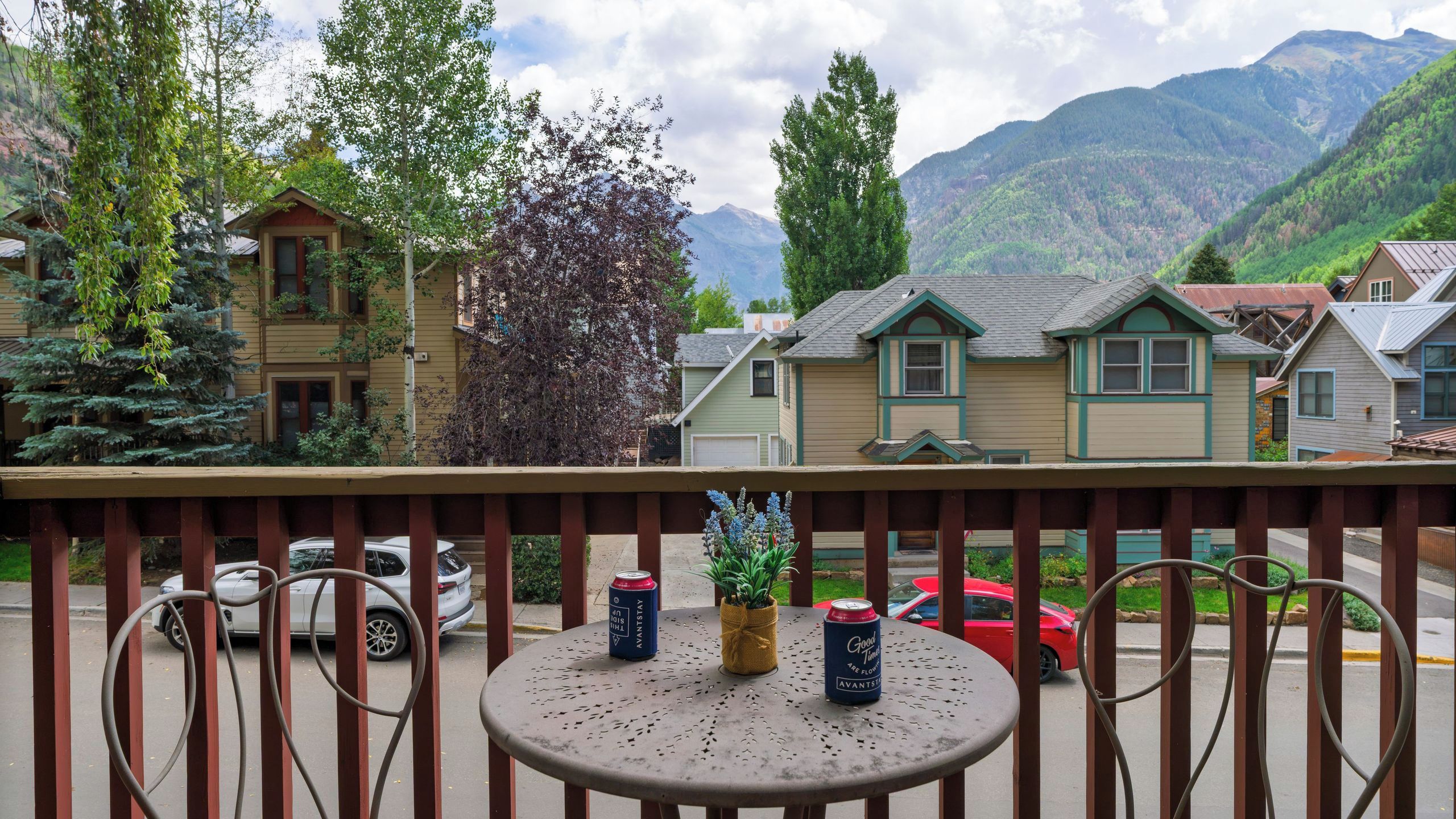 A balcony with a table, chairs, and a view of houses and mountains.