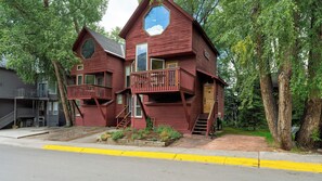 A two-story wooden cabin with a balcony, a large window, and a door.