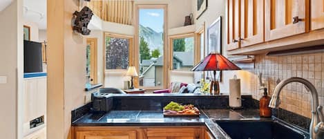 A kitchen with wooden cabinets, a marble countertop, a red lamp, and a view of mountains through the windows.
