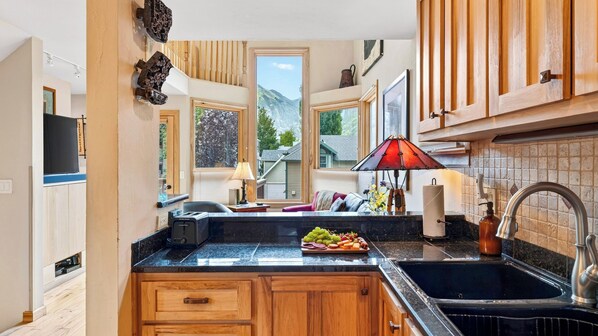 A kitchen with wooden cabinets, a marble countertop, a red lamp, and a view of mountains through the windows.