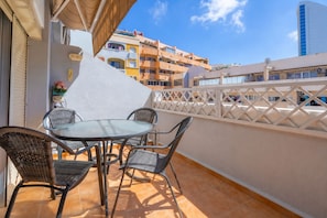 Ein Balkon mit rundem Tisch und vier Stühlen, einem weißen Zaun und Gebäuden im Hintergrund.