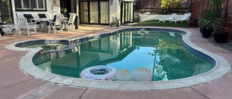 A swimming pool with a curved edge, surrounded by a patio area with chairs and a table.