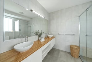 Un baño moderno con tocador de madera, un espejo grande, un lavamanos blanco y una cabina de ducha con paredes de vidrio.