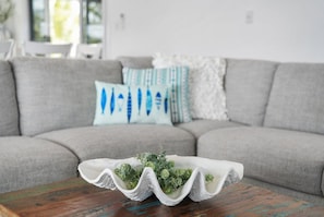 Una sala de estar con un sofá gris, una mesa de centro de madera y cojines decorativos.