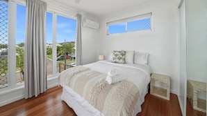 Quarto com cama, ventilador de teto, janela com vista e uma mesinha de cabeceira.