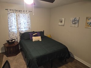 Een slaapkamer met een bed, een nachtkastje, een raam met gordijnen en decoratie aan de muur.