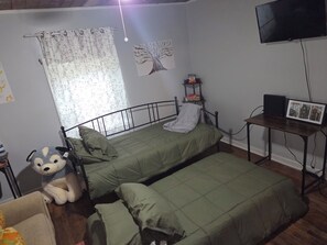 A bedroom with two beds, a small table, a TV, and a teddy bear.