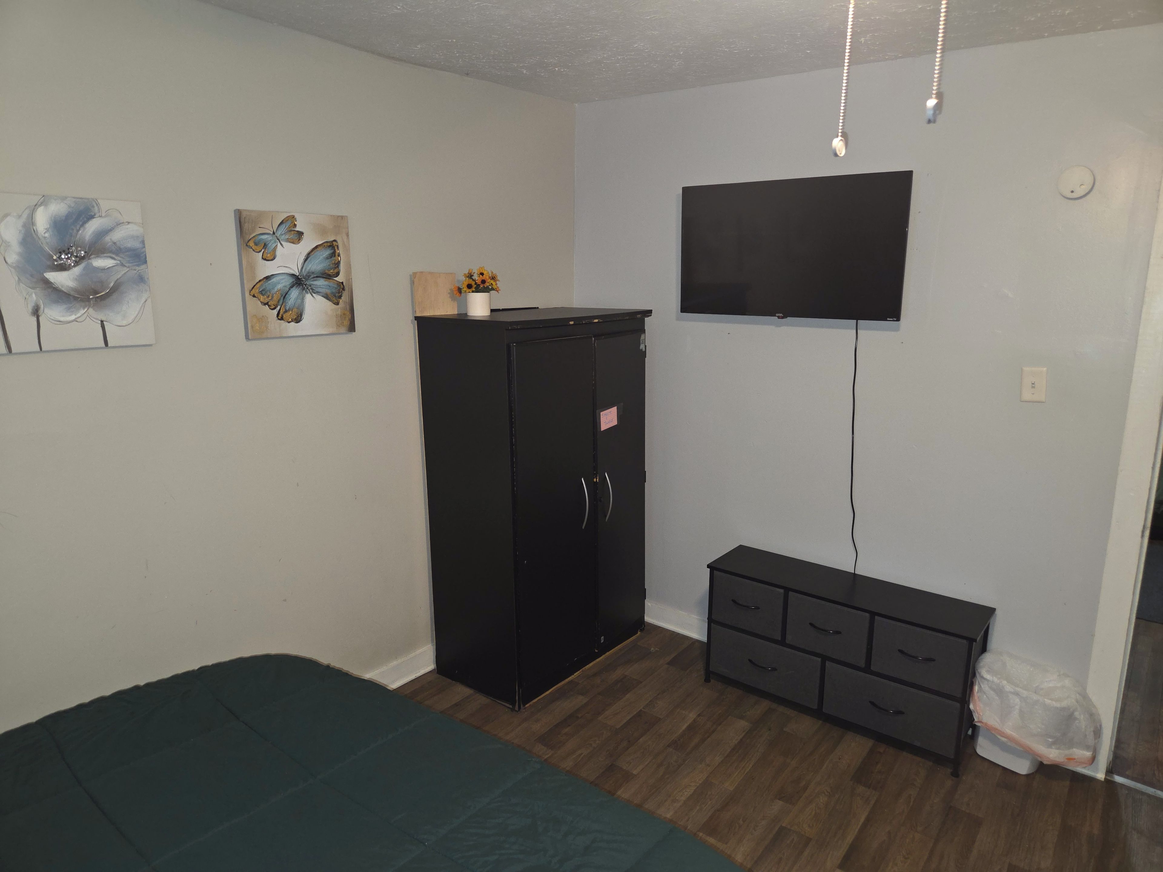 A bedroom with a bed, a wardrobe, a TV mounted on the wall, and artwork on the wall.