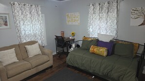 A room with a sofa, a bed with floral pillows, a desk with a chair, and a ceiling fan. - Yellow Mellow sleeps 4  (Jackson)