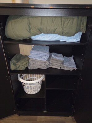 A storage unit with shelves containing folded towels and a laundry basket.