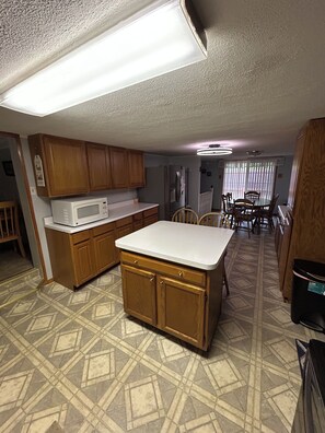 A compact kitchen with wooden cabinets, a microwave, and a dining area with chairs and a table.