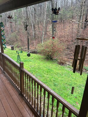 A wooden deck with a railing, overlooking a grassy yard with various wind chimes and a windmill.