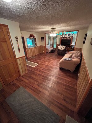 A room with a wooden floor, a sofa, a television, and a ceiling fan. - Granny's Creekside Lodge 3-bedroom with WiFi & AC in charming Bluefield (Bluefield)