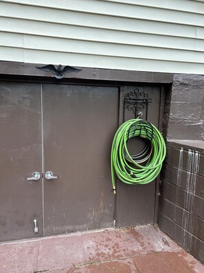 A brown garage door with a green garden hose coiled on a metal hook.