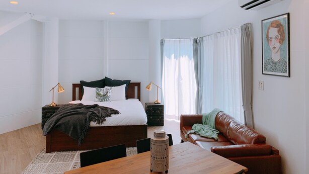 Ein Schlafzimmer mit einem Bett, Nachttischen, einem Schminktisch, einem braunen Ledersofa, einem Holztisch und einem Fenster mit Vorhängen.