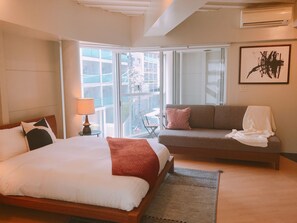 Habitación de hotel con cama, sofá, balcón con vistas y un cuadro en la pared.