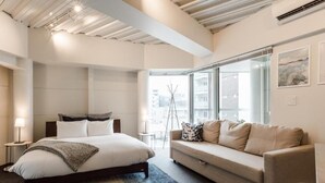 Ein modernes Hotelzimmer mit einem großen Bett, einer Sitzecke, einem kleinen Tisch und einem Fenster mit Blick auf die Stadt.