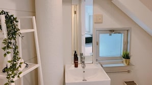 Ein Badezimmer mit einem weißen Waschbecken, einem Spiegel, einer Topfpflanze und einem Fenster.