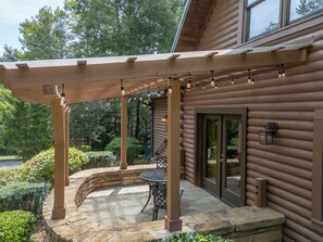 Una pergola in legno con luci a tendina, un patio in pietra e una porta vetrata che dà su un'area coperta.