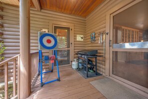 Eine Holzhütte mit Veranda, einem auf einem Ständer stehenden Zielscheibe, einem Grill und einer Tür mit einem Warnschild.