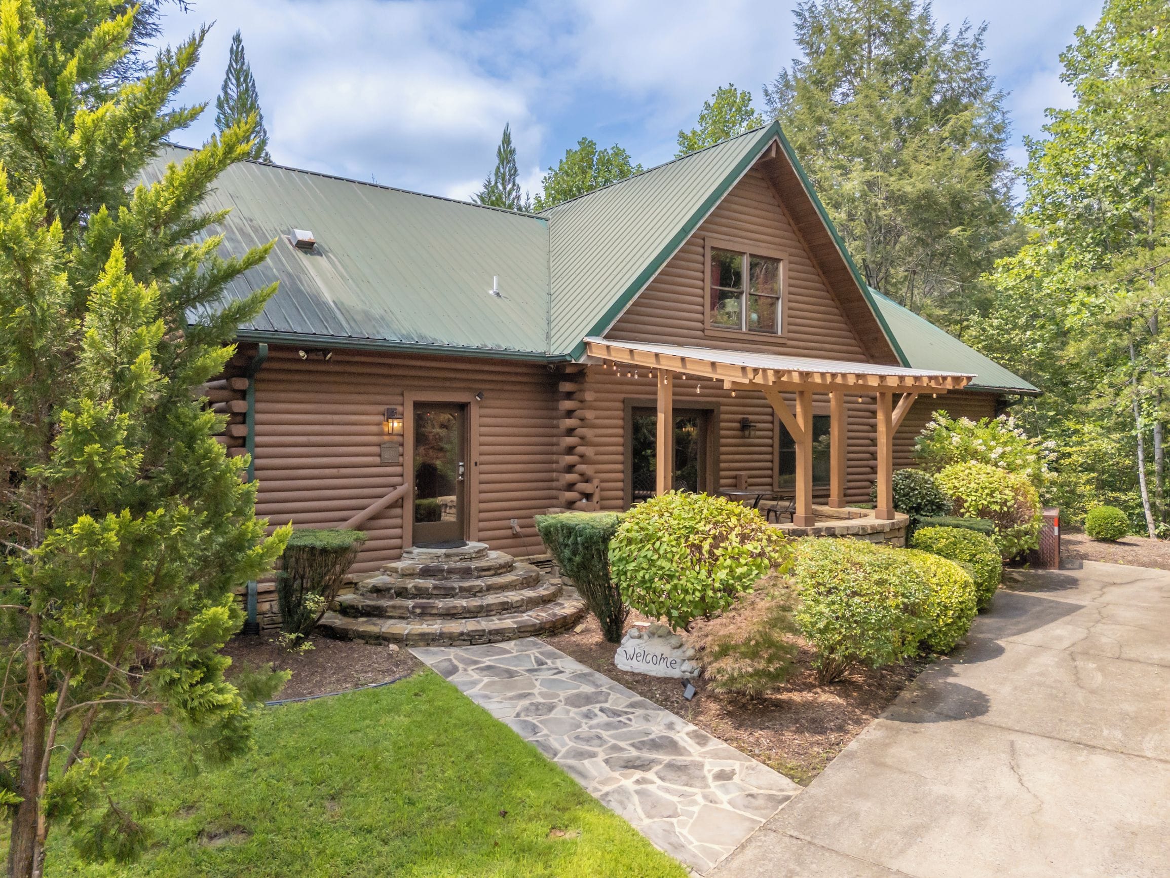 A log cabin with a stone pathway leading to the entrance, surrounded by greenery and trees.