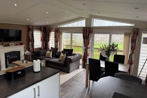 A spacious living area with a fireplace, a sofa set, a dining table with chairs, and large windows offering a view of the outdoors.