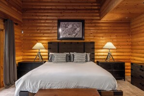 Ein Schlafzimmer in einer Blockhütte mit einem großen Bett, zwei Nachttischen, einem gerahmten Bild an der Wand und einer Holzbalkendecke.