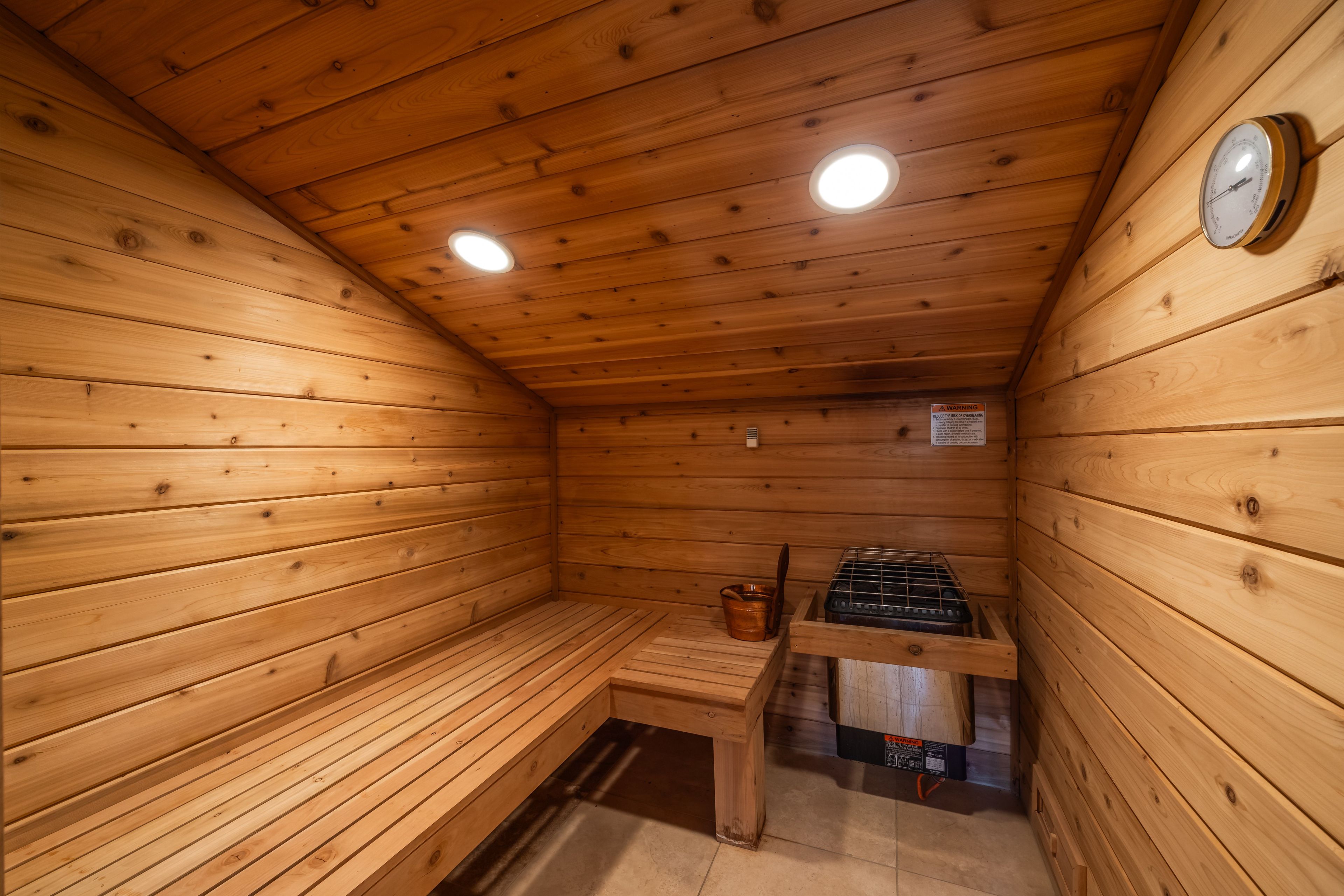 Un sauna en bois avec des bancs, un chauffage et une horloge au mur.