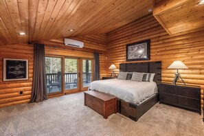Ein Schlafzimmer in einer Blockhütte mit einem Bett, Nachttischlampen, einer gerahmten Patentzeichnung und Blick durch eine Glastür auf eine Außenterrasse.