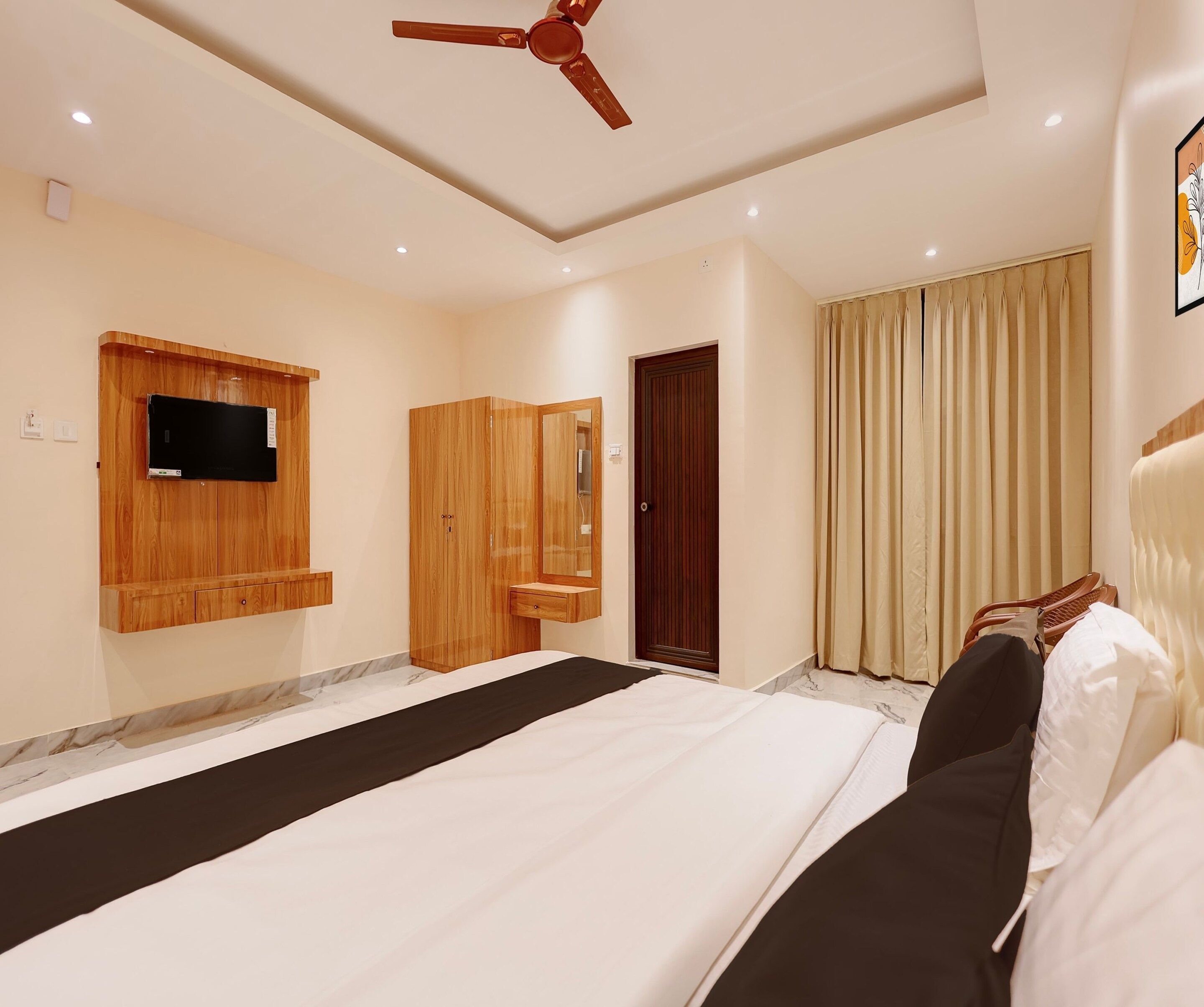 Une chambre d’hôtel avec un lit, un téléviseur fixé au mur, une armoire en bois, une porte et une fenêtre avec des rideaux.