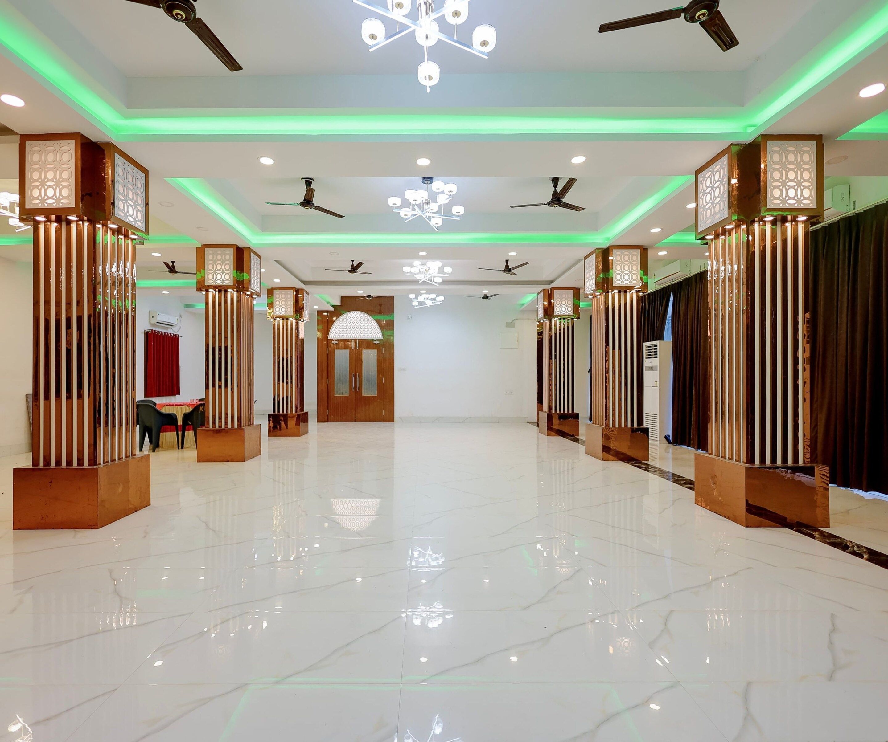 A hotel lobby with a marble floor, ceiling fans, decorative light fixtures, and a central chandelier.