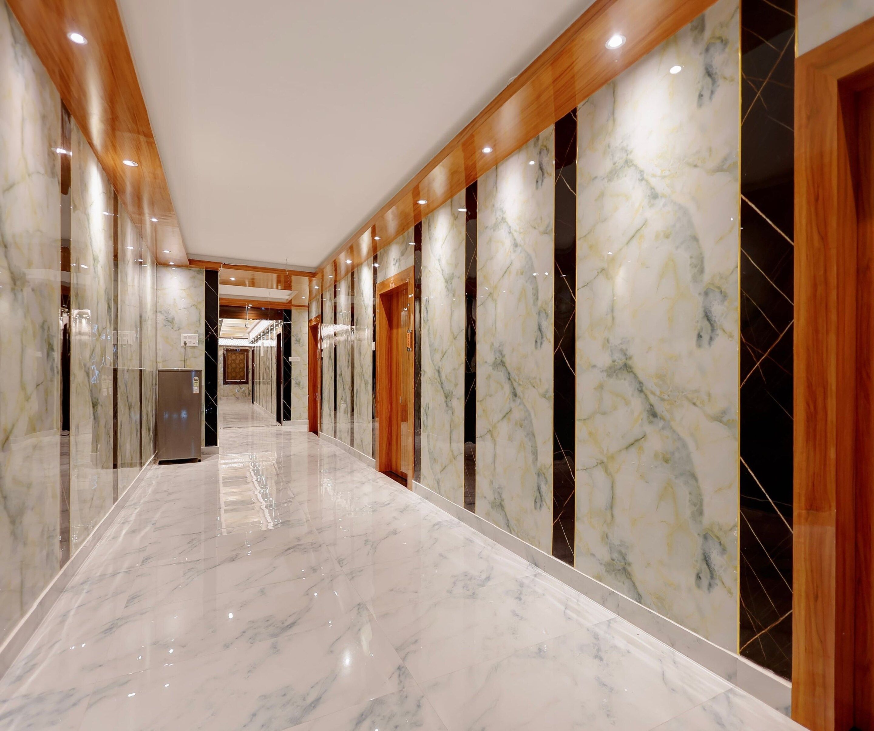 A corridor with marble flooring and wooden paneling, leading to a room with a large mirror and a door.