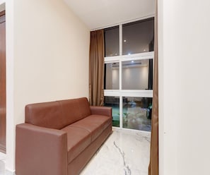 A room with a brown leather sofa, a large window with curtains, and a marble floor. - Deluxe Kamala Resort (Bhubaneshwar)