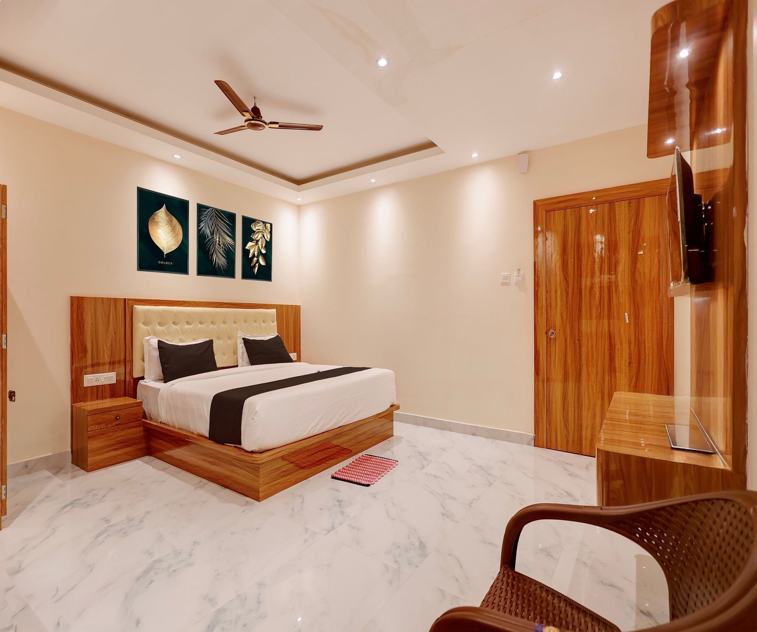 A modern bedroom with a large bed, wooden headboard, a ceiling fan, and a TV mounted on the wall.