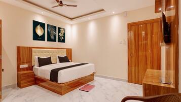 A modern bedroom with a large bed, wooden headboard, a ceiling fan, and a TV mounted on the wall.