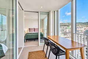 A modern bedroom with a bed, a wooden table, and a view of a cityscape. - Hyde Lane Stay - 3BR with Pool, Gym & Views (Wellington)
