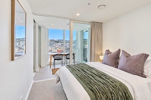 A hotel room with a large bed, a desk, and a view of the city. - Hyde Lane Stay - 3BR with Pool, Gym & Views (Wellington)