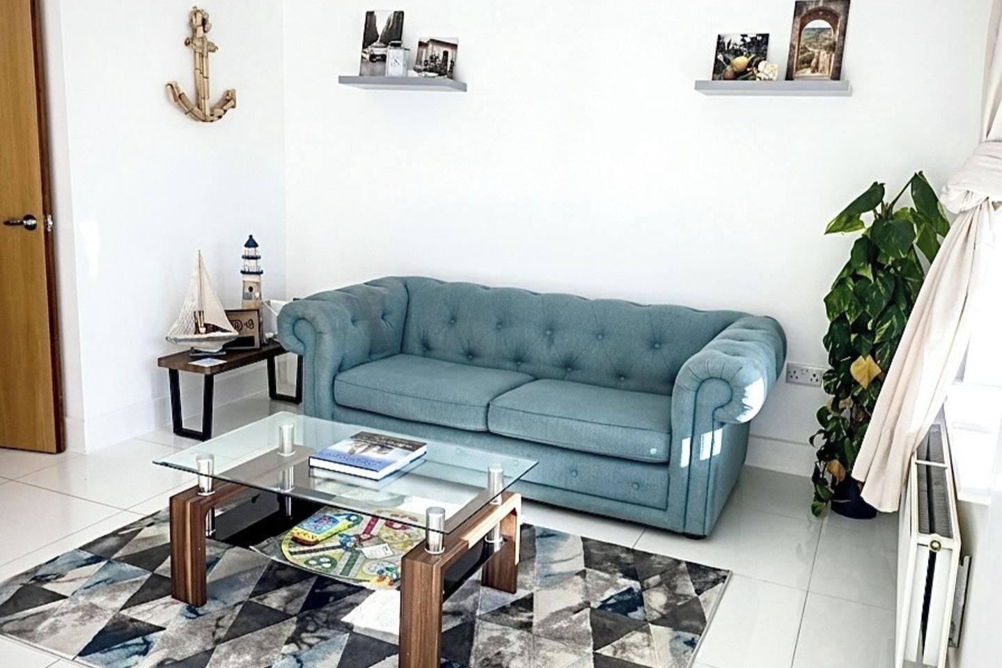 A living room with a blue sofa, a glass coffee table, and a patterned rug.