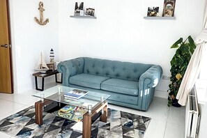 A living room with a blue sofa, a glass coffee table, and a patterned rug.