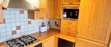A compact kitchen with a gas stove, a microwave, wooden cabinets, and a tiled backsplash.