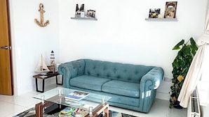 Una sala de estar con un sofá azul, una mesa de centro de vidrio, un tapete estampado y un ventilador de techo.