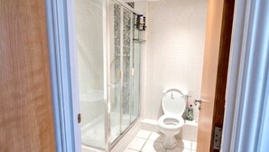 Baño con cabina de ducha de vidrio, inodoro y suelo de baldosas.