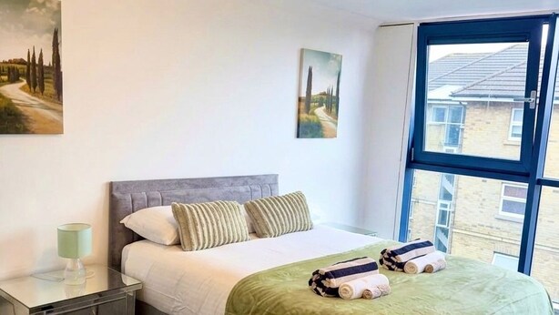Un dormitorio con cama, mesita de noche, lámpara y obras de arte en las paredes.