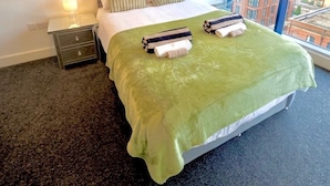 Habitación de hotel con una cama grande, una mesita de noche, una lámpara y dos cuadros en la pared.
