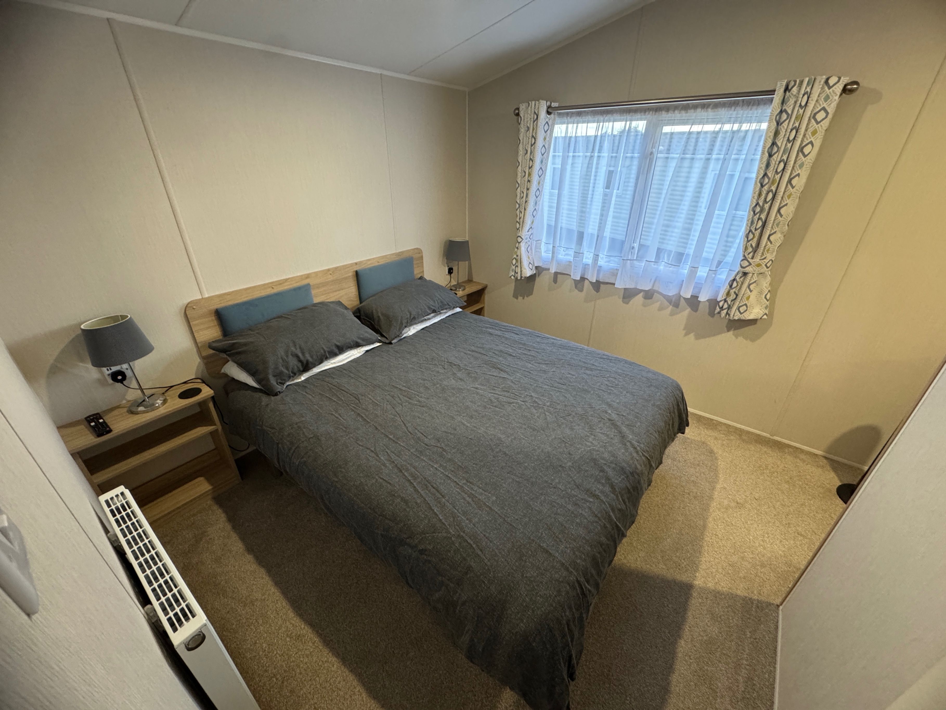 Un dormitorio con cama, lámparas de noche, un calentador y una ventana con cortinas.