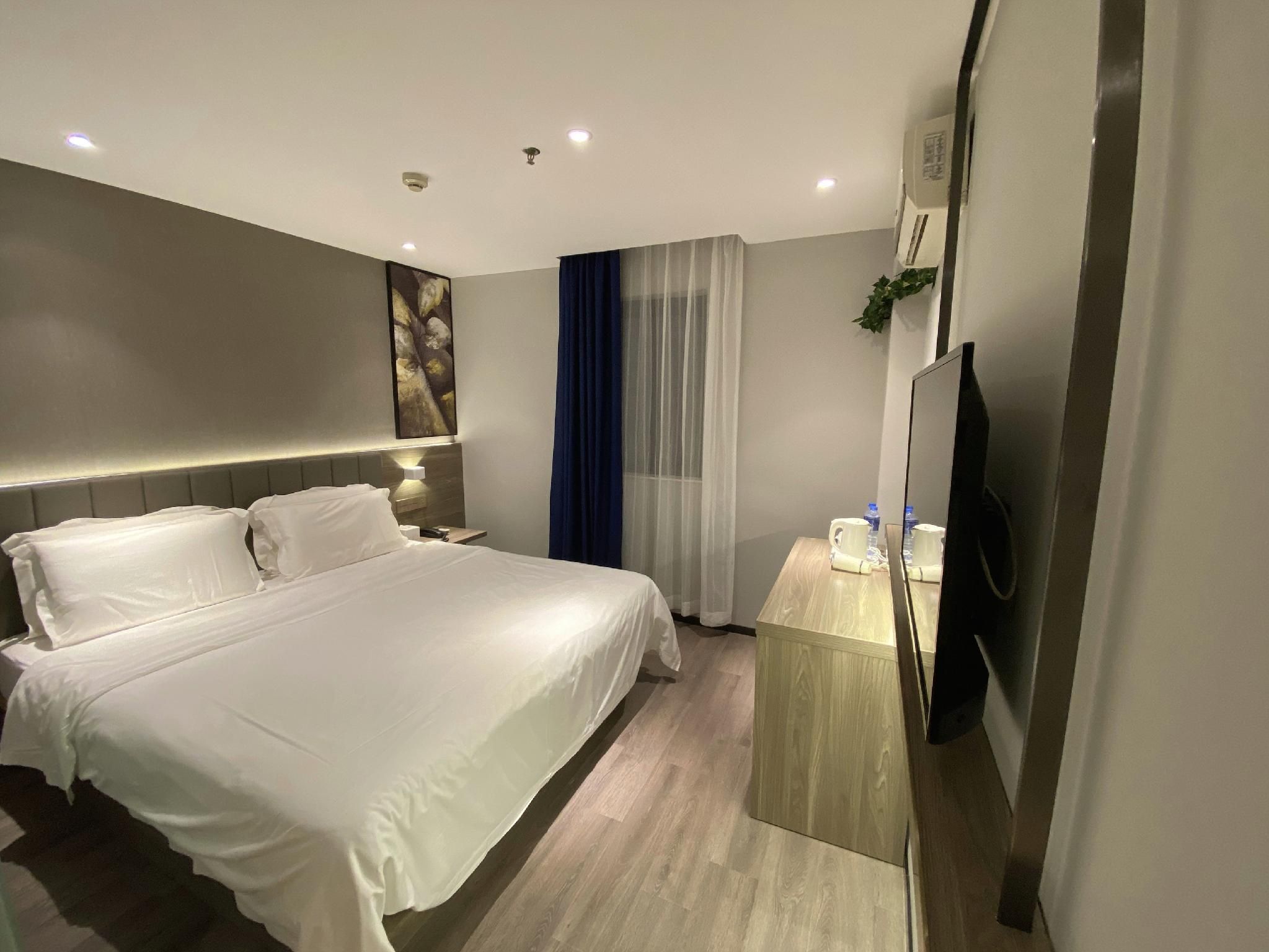 A modern hotel room with a large bed, bedside tables, a flat-screen TV, and a window with curtains.