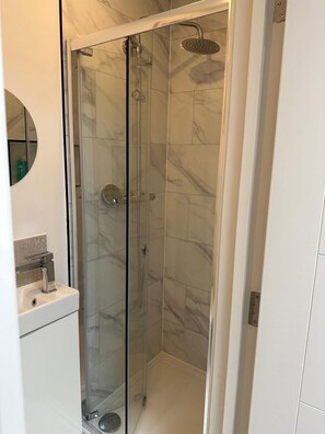Eine Duschkabine mit Glaswänden, einer Handbrause und einem am Wand montierten Wasserhahn.